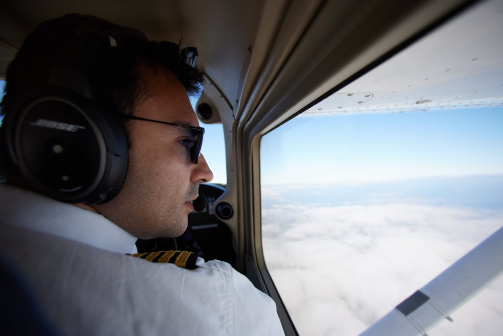 extra close up side profile shot of male pilot looking out window while in the clouds. with gold stripes on uniform and wearing bose headphones
