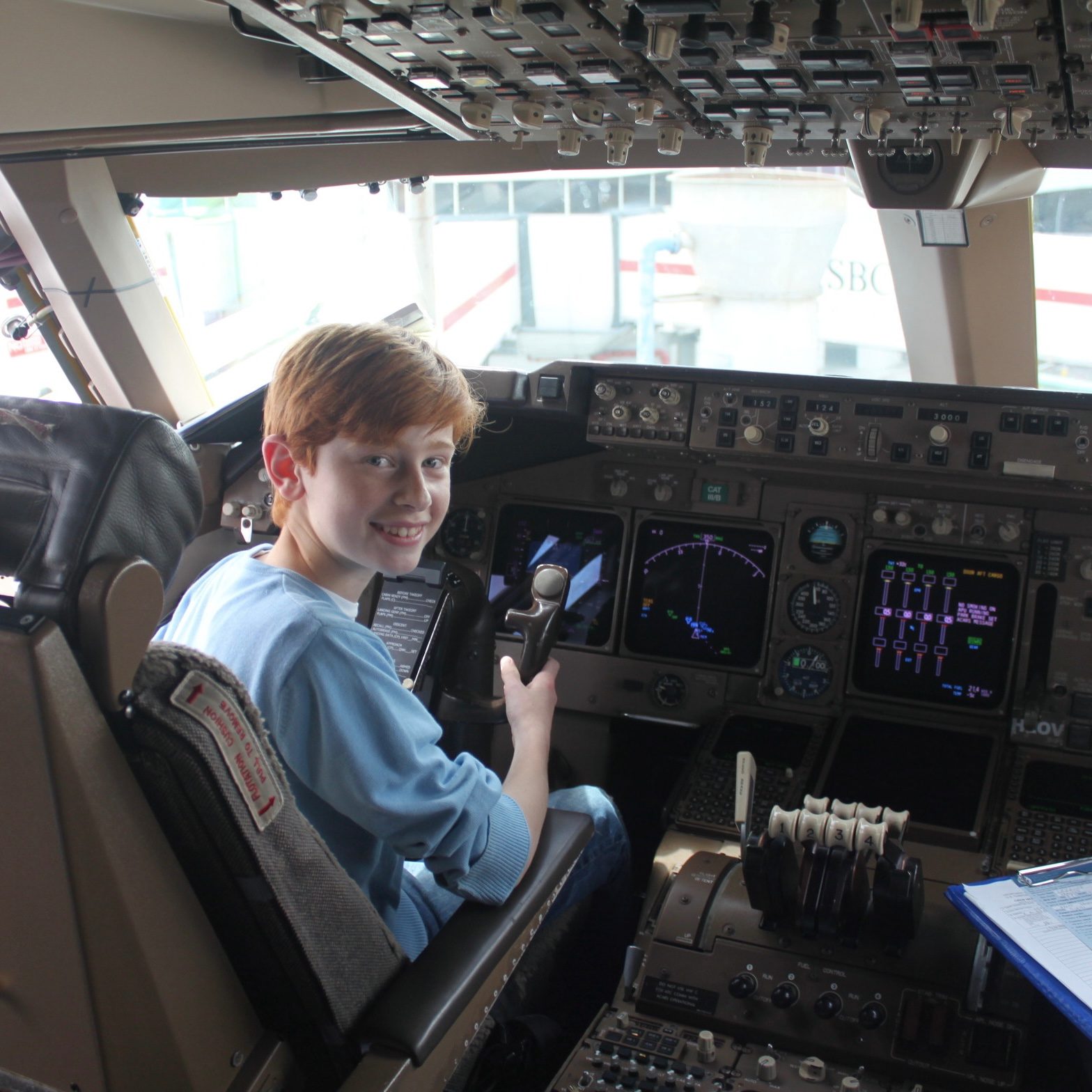 Young Adrien sitting in the cockpit of an airliner holding Yoke