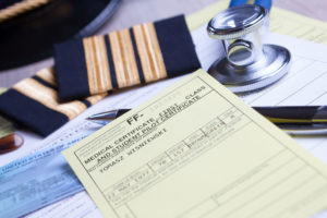 Close up of an airplane pilot equipment hat and epaluetes with medical and pilot certificate, stethoscope and pen. Conceptual image of medical exam.