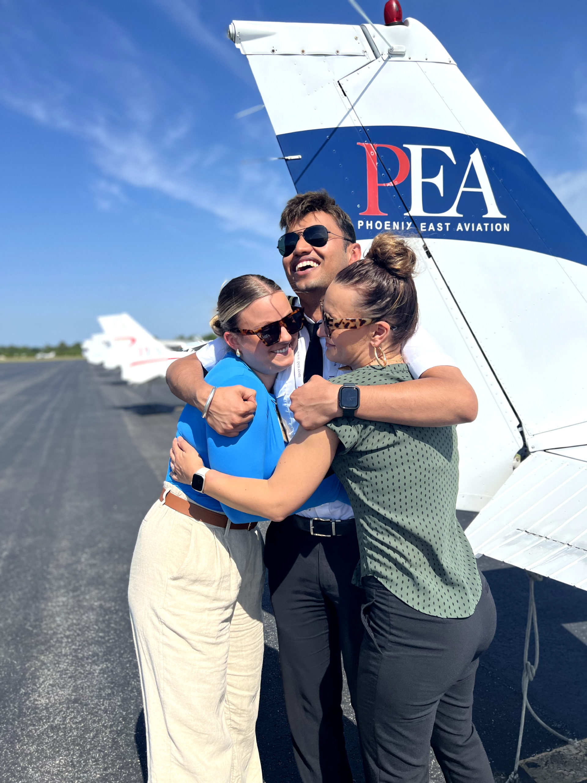 Sara Mohlin (R), Tegvir Anand (M), and Amelie Coleman(R) hugging in front of PEA Cessna 172 tail on KFIN tarmac during Teg_s last day at PEA