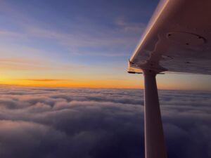 above clouds during sunset, looking outside of cessna 172 window