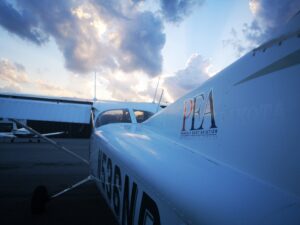 a plane on ground with a building and a cloudy sky behind it.
