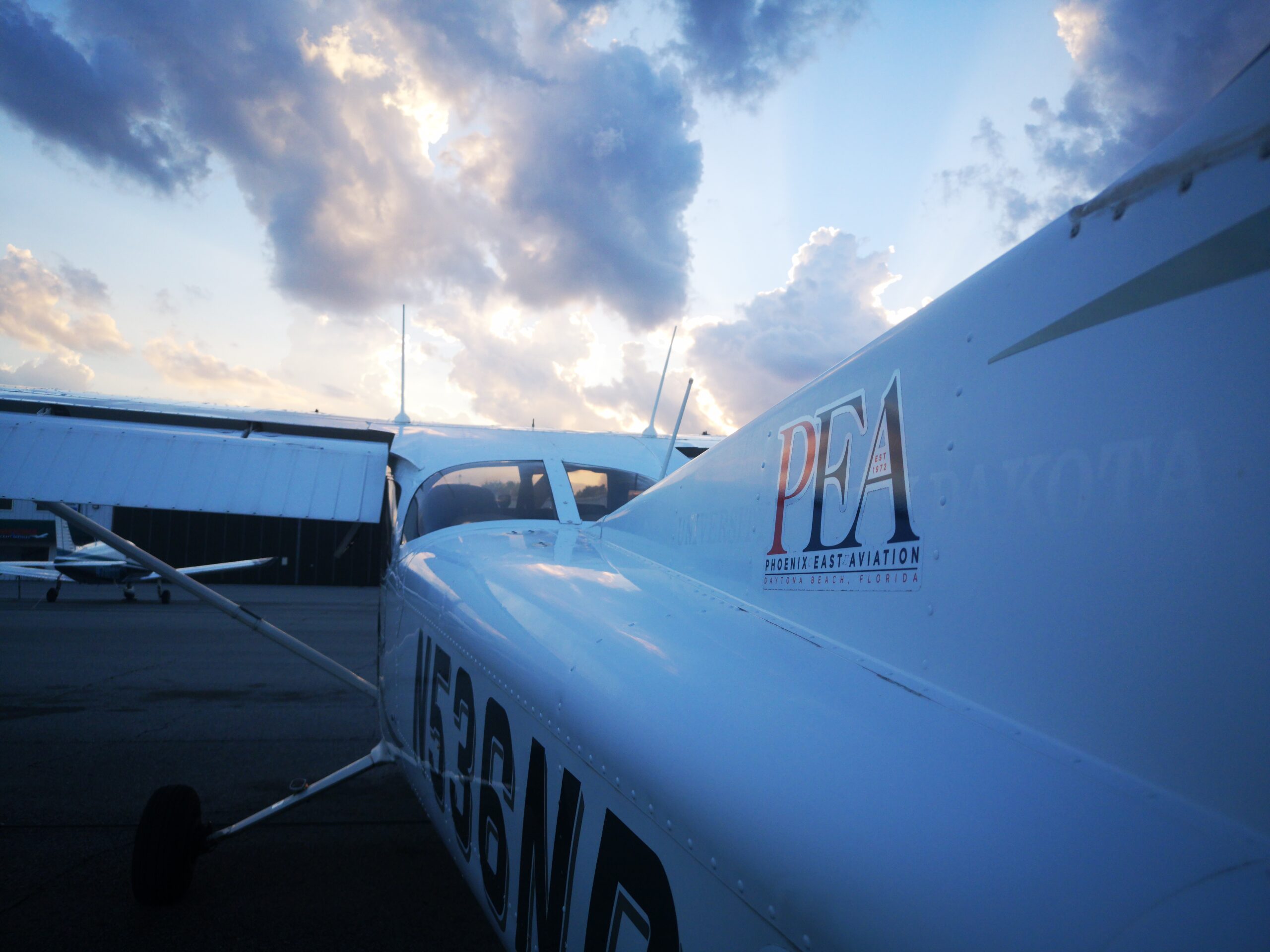 a plane on ground with a building and a cloudy sky behind it.