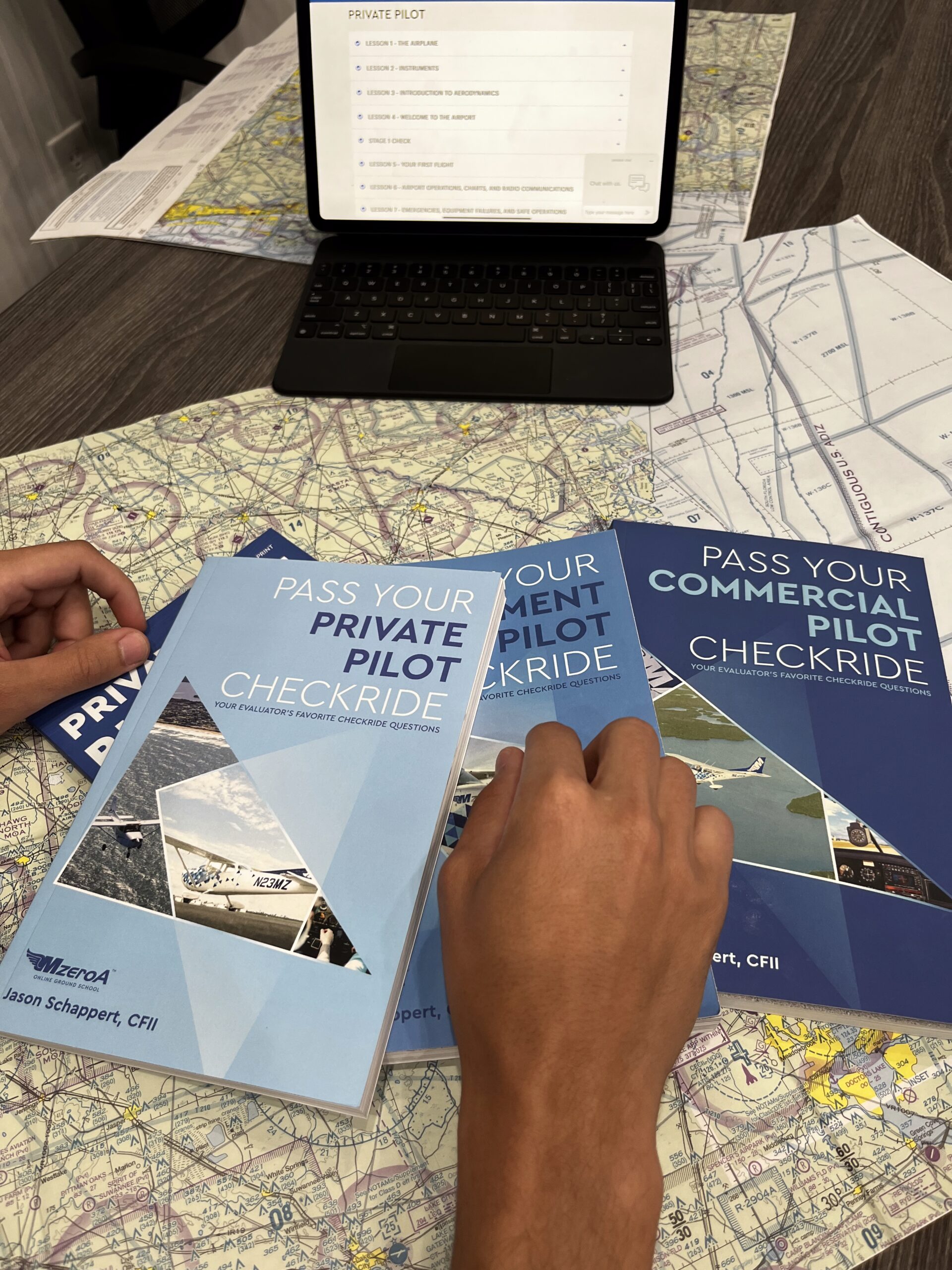 a stack of booklets: "Pass Your Private Pilot Checkride" and "Pass Your Commercial Pilot Checkride"