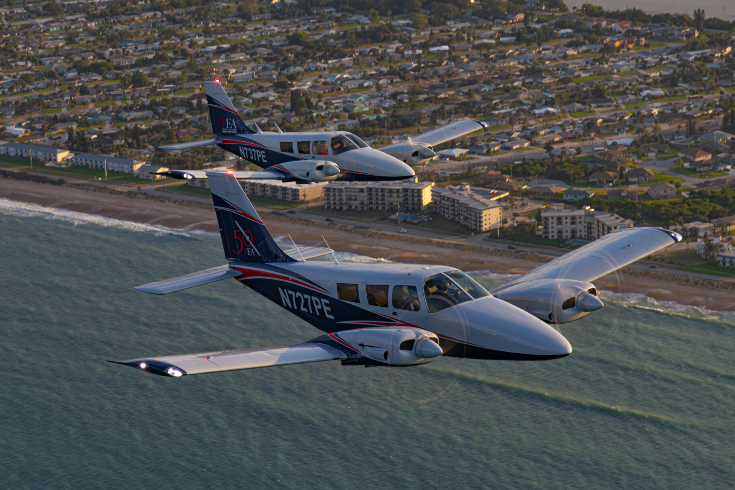 Two Piper Seneca training aircraft flying in formation along the coastline during a sunset training flight.